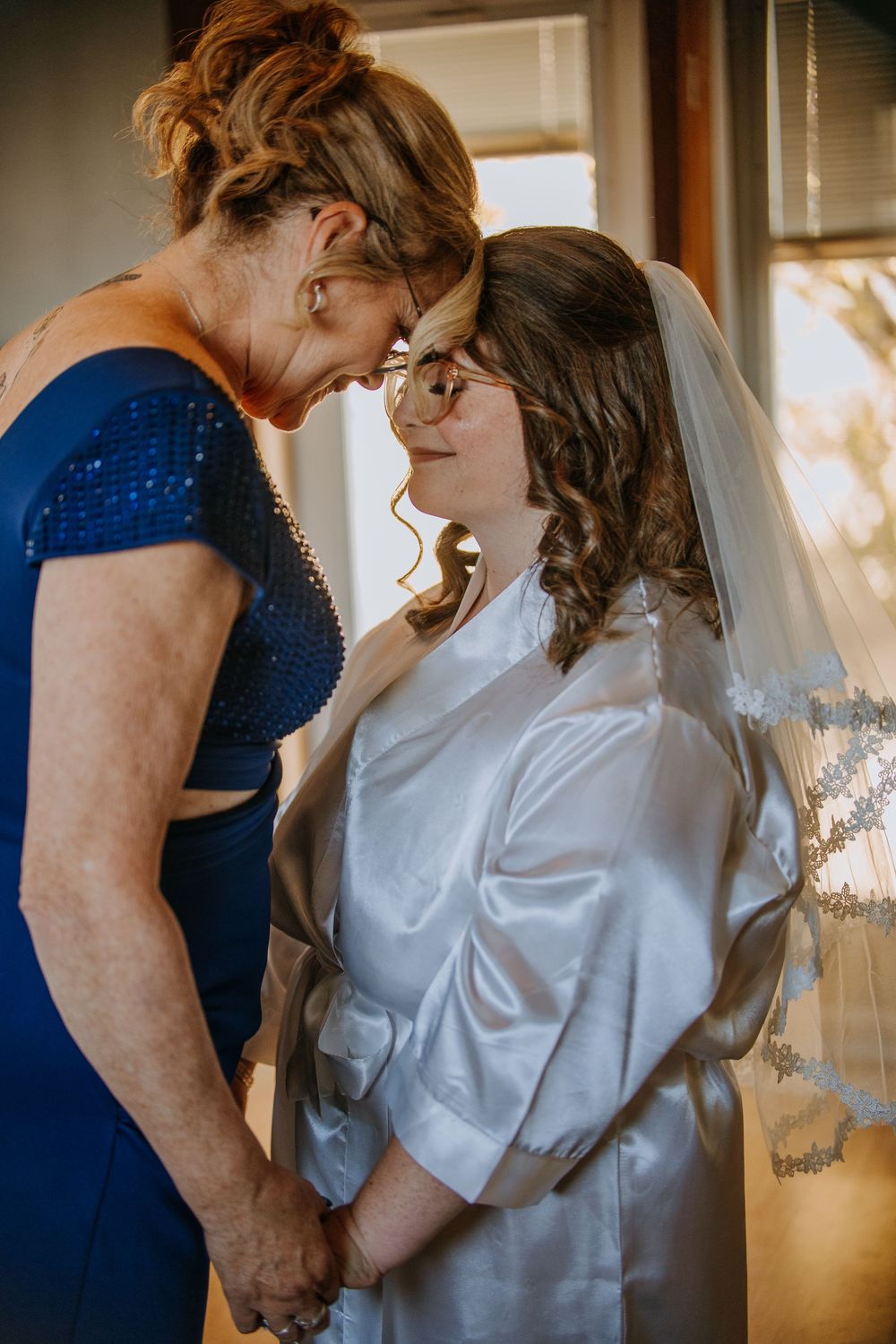 Couple in navy blue and white outfits share intimate moments in a sunlit room by a window.