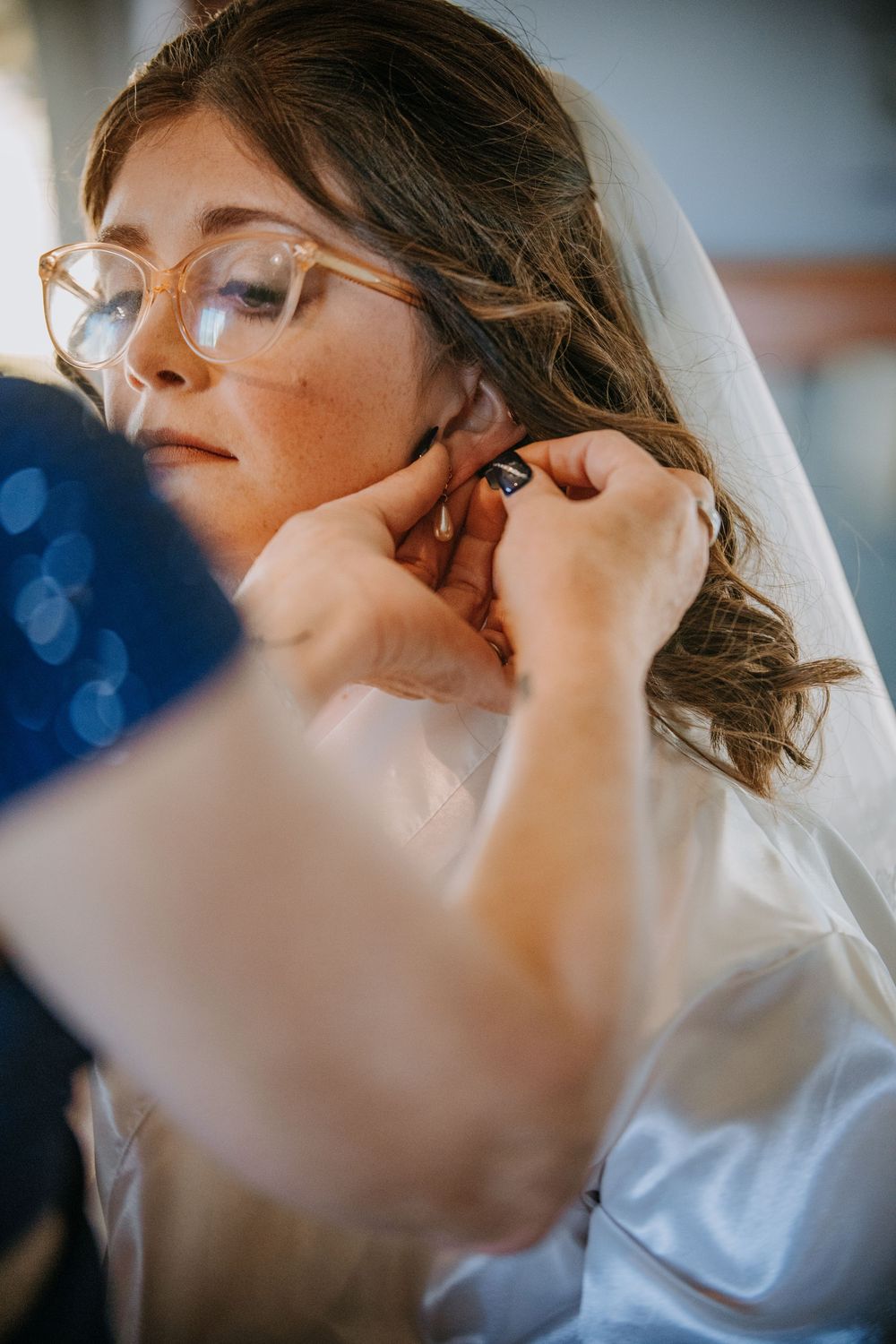 A makeup artist applies eye shadow to a bride during wedding preparation in soft natural light.