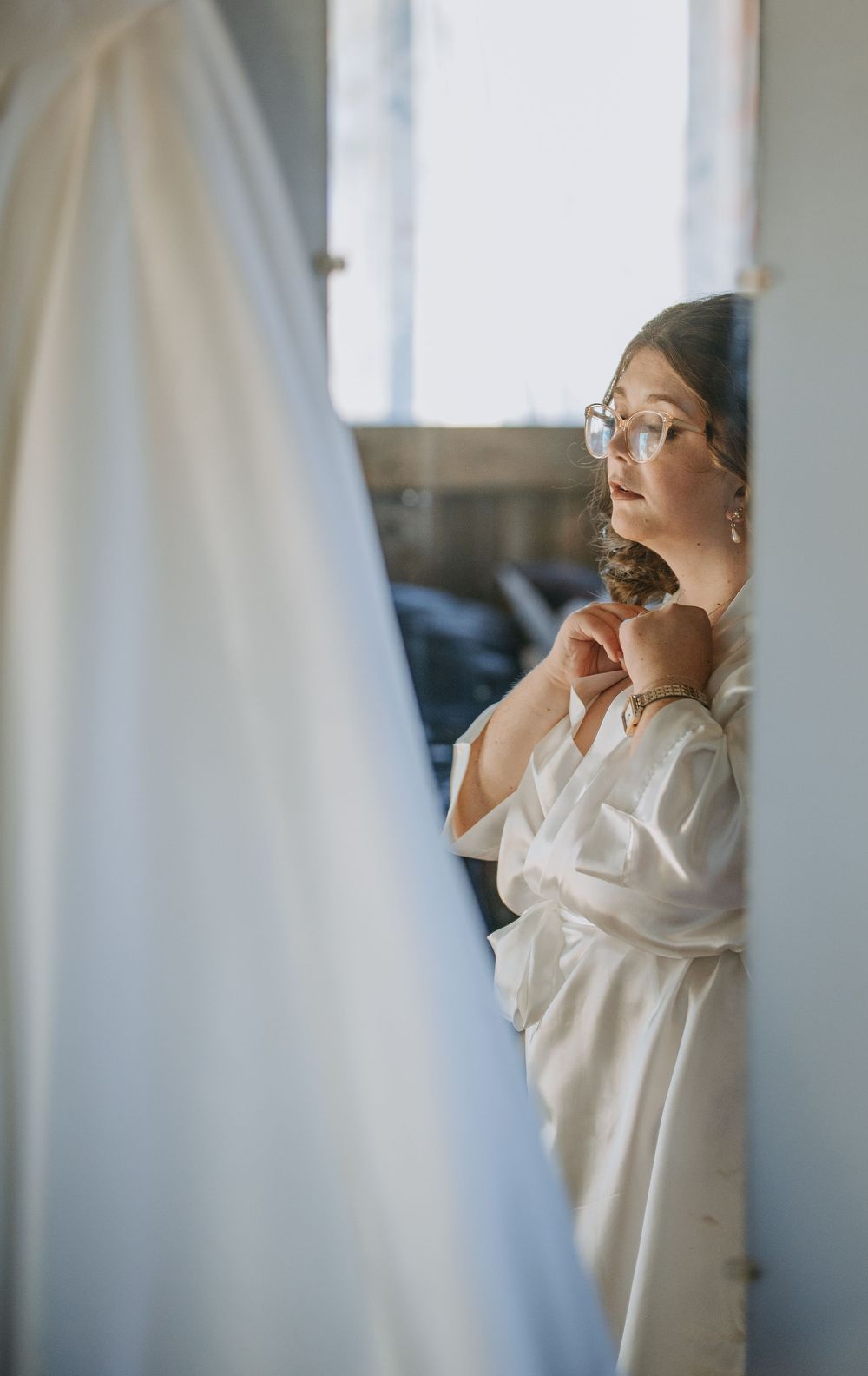 A person in a white silk robe gazes thoughtfully through sheer curtains in soft natural light.