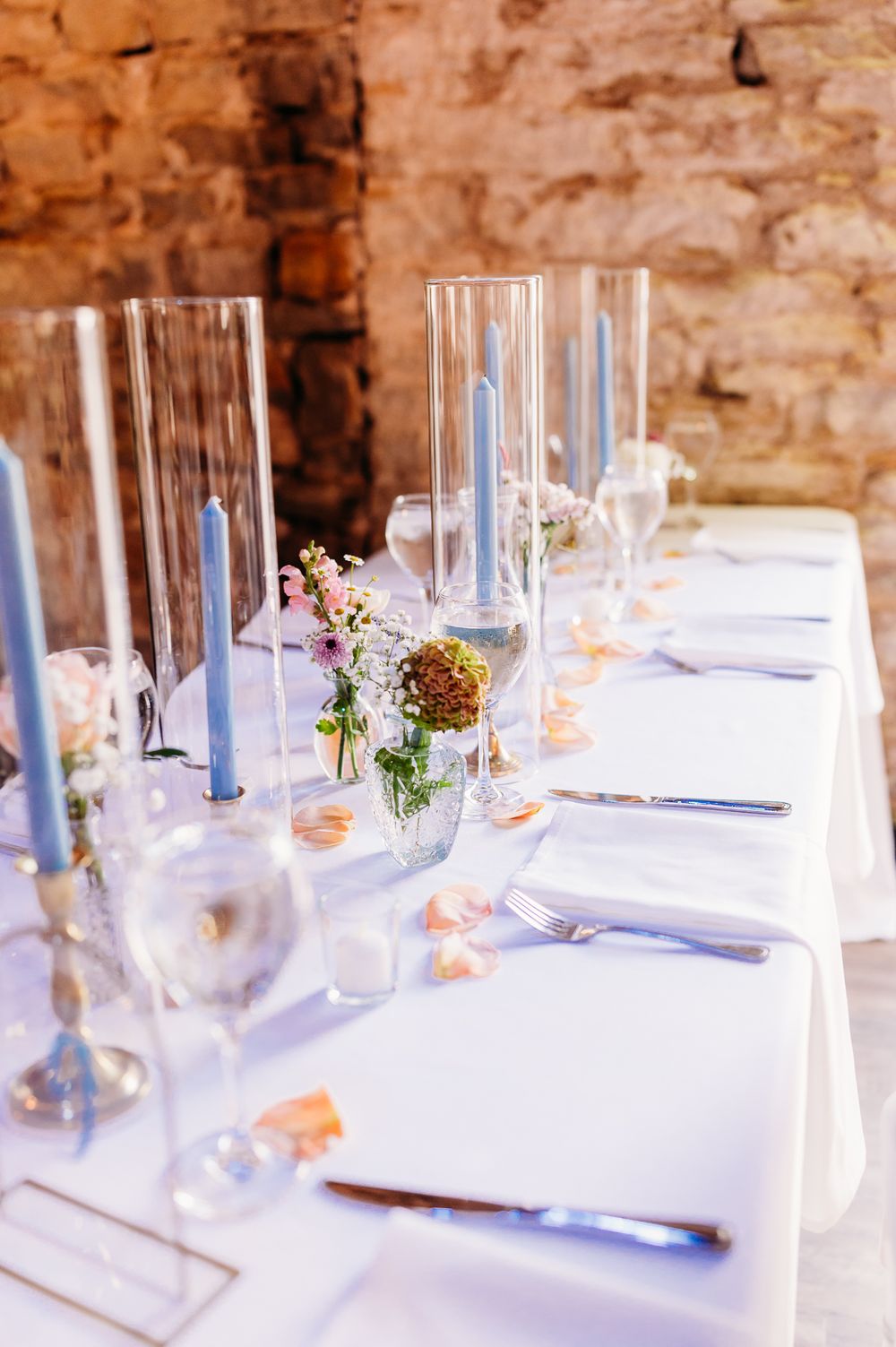 Elegant wedding table setting with tall glass centerpieces and delicate floral arrangements.