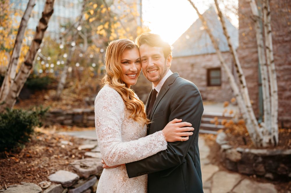 Two people share a romantic embrace at sunset with fall foliage in the background.
