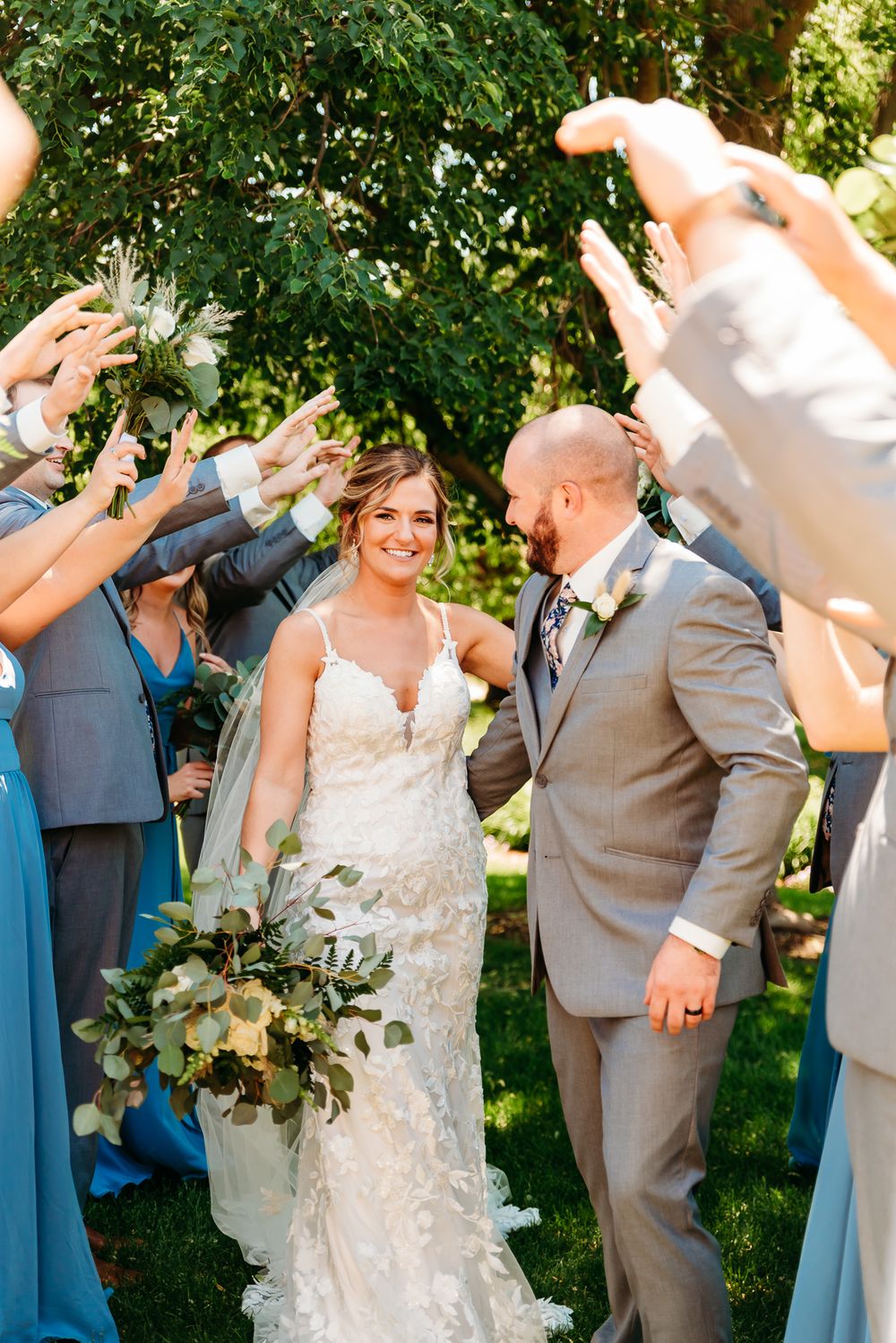 Wedding couple walking through guest tunnel with raised arms in outdoor celebration.