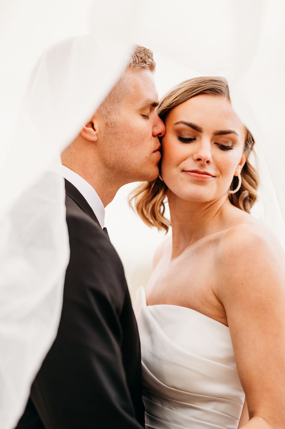 Intimate wedding portrait through sheer veil showing tender moment between newlyweds.