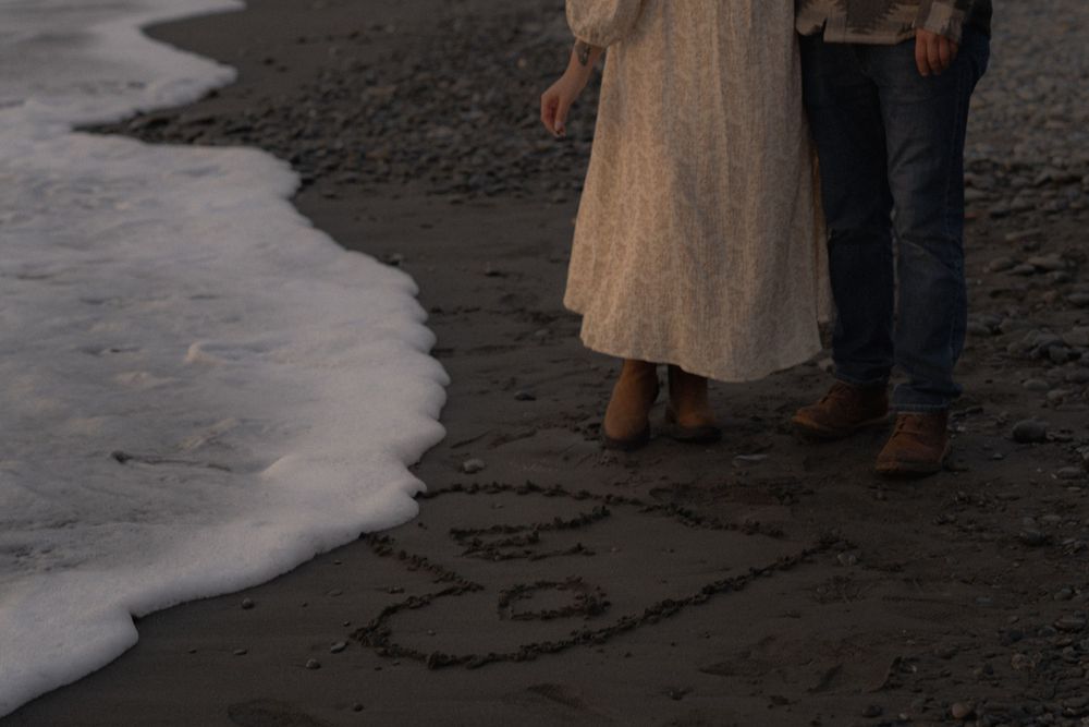 Ocean waves meet footprints and drawings in the dark sand at sunset. on Ruby Beach, Olympic National Park.