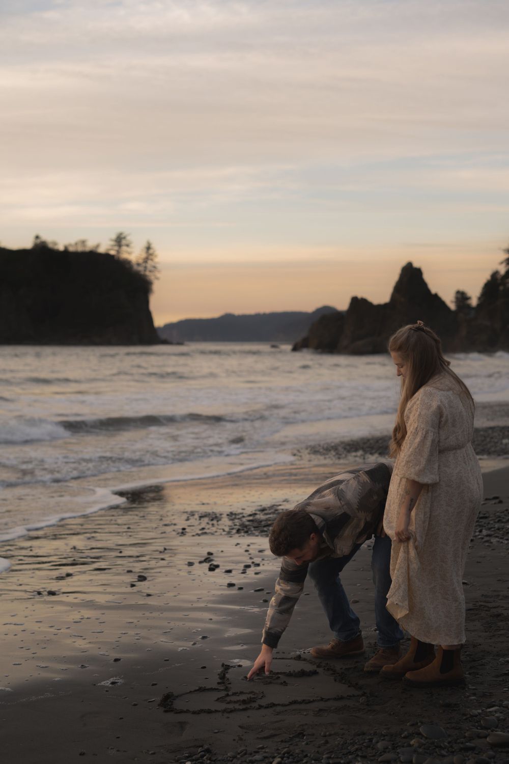Couple drawing in the sand on a moody Pacific Northwest beach at sunset on Ruby Beach, Olympic National Park.