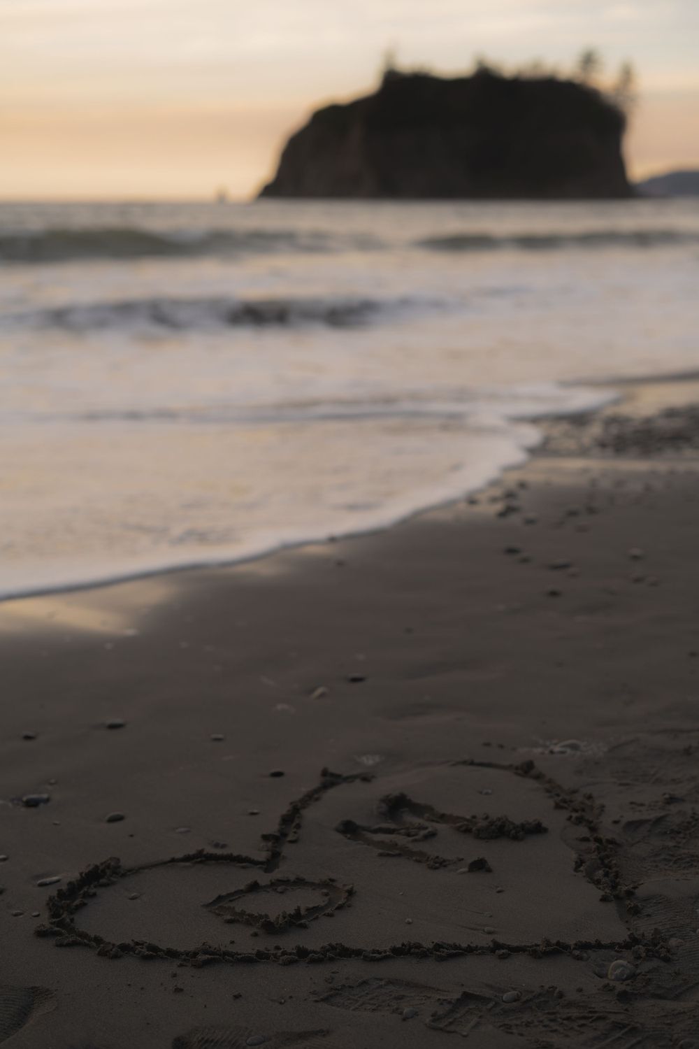 Heart drawn in sand on beach with dramatic rocky coastline silhouette at sunset on Ruby Beach, Olympic National Park.
