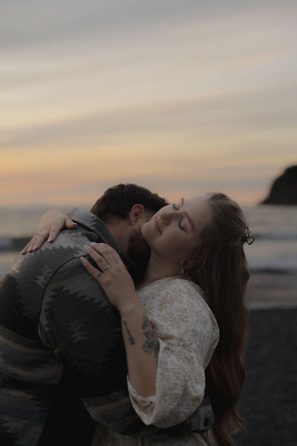 Intimate embrace between couple in white lace and dark clothing against sunset beach backdrop on Ruby Beach, Olympic National Park.