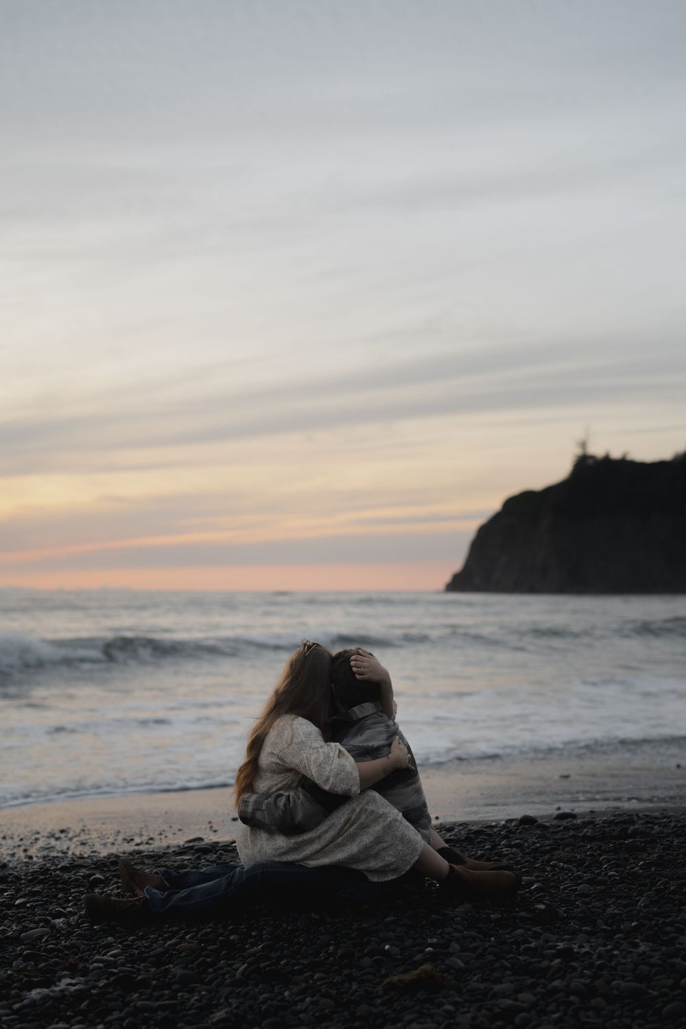Couple cuddled together watching sunset from black sand beach with coastal cliff backdrop on Ruby Beach, Olympic National Park.