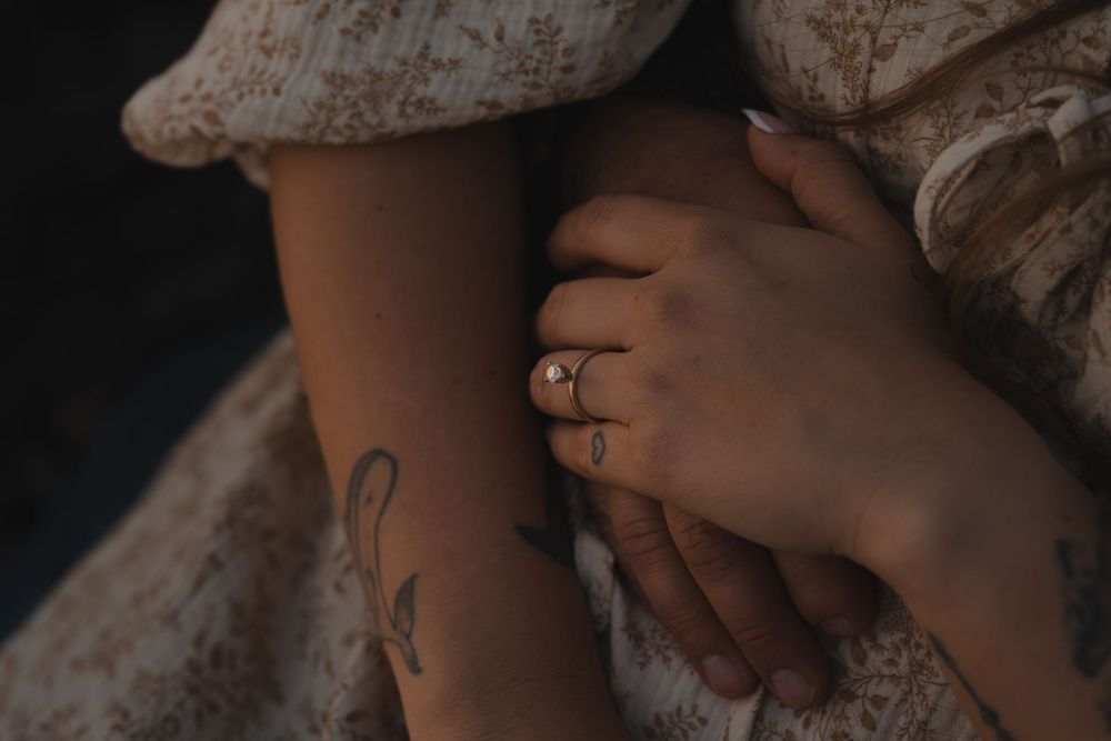 Close-up of hands with engagement ring and delicate tattoo detail on lace fabric on Ruby Beach, Olympic National Park.
