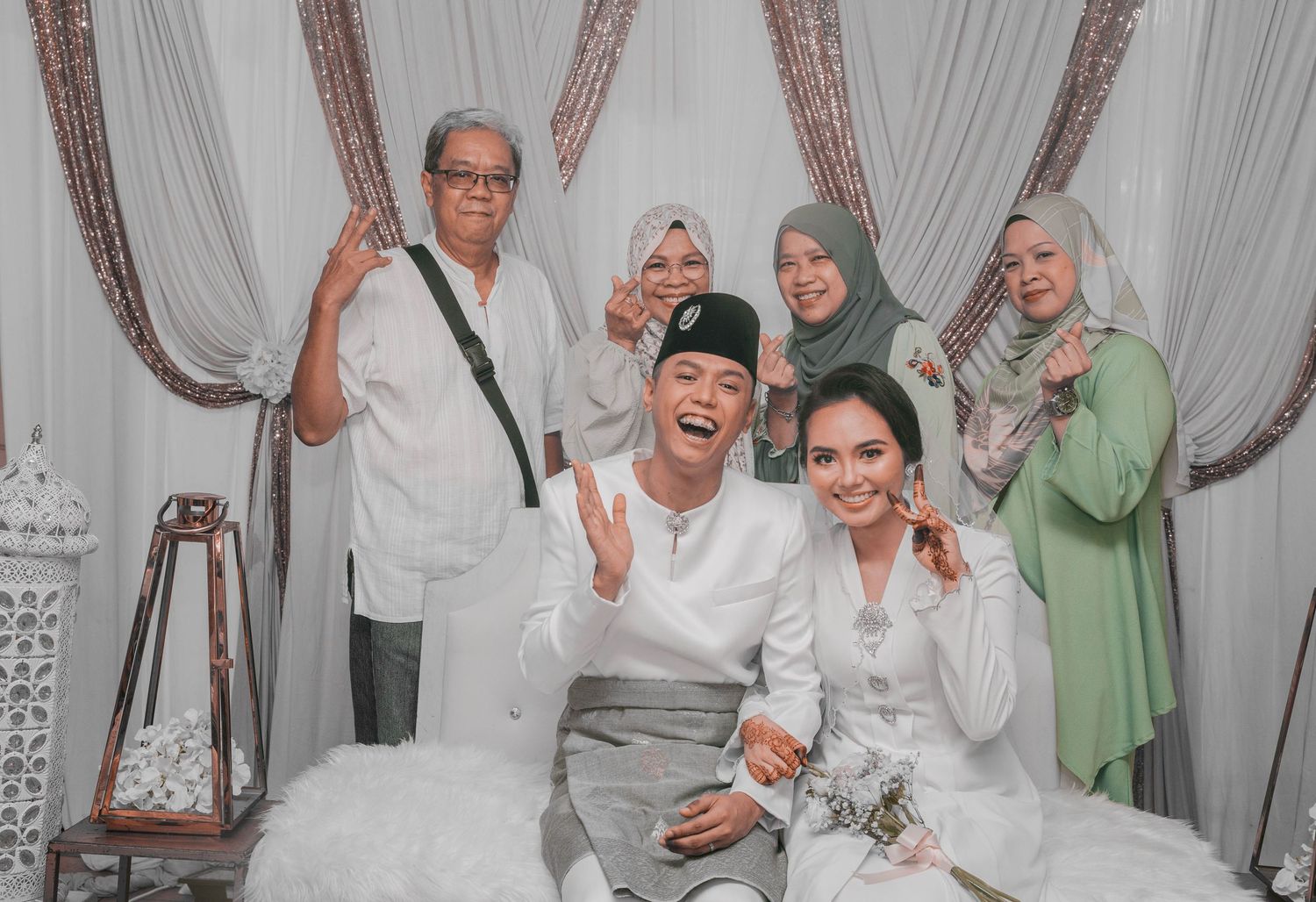 A celebratory wedding group photo with family members in traditional Malay attire.