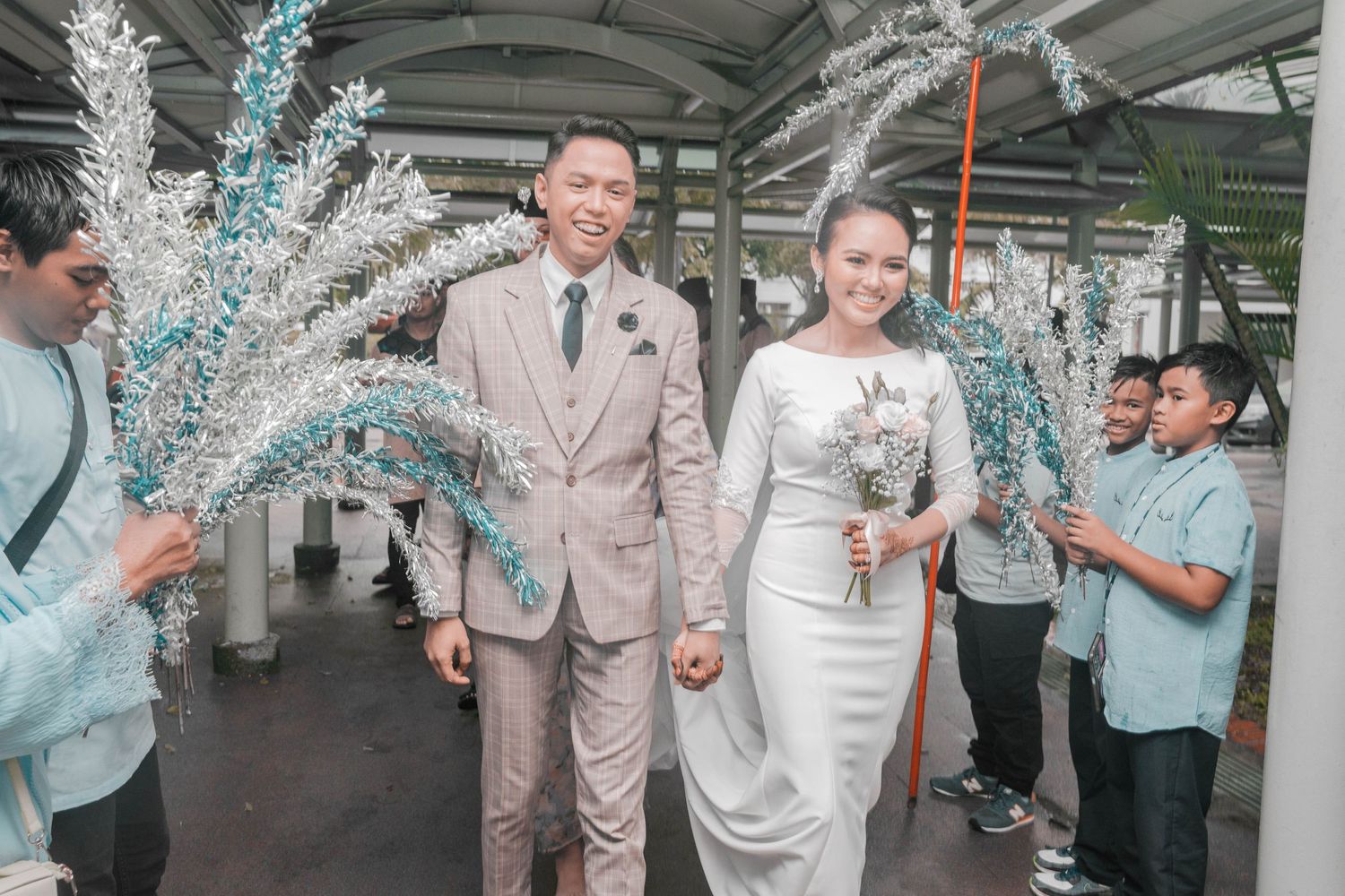 A couple walks through a corridor decorated with blue and white floral arrangements at their wedding celebration.