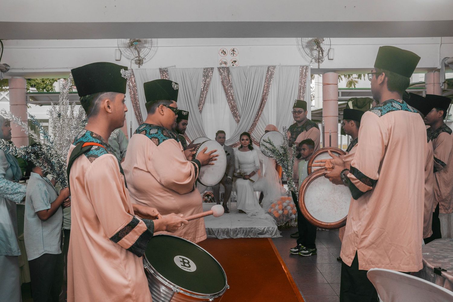 Traditional musicians in peach-colored uniforms and black hats perform at an indoor celebration.