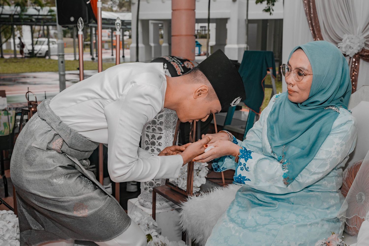 A traditional Malay wedding ceremony with henna application taking place against a modern backdrop.