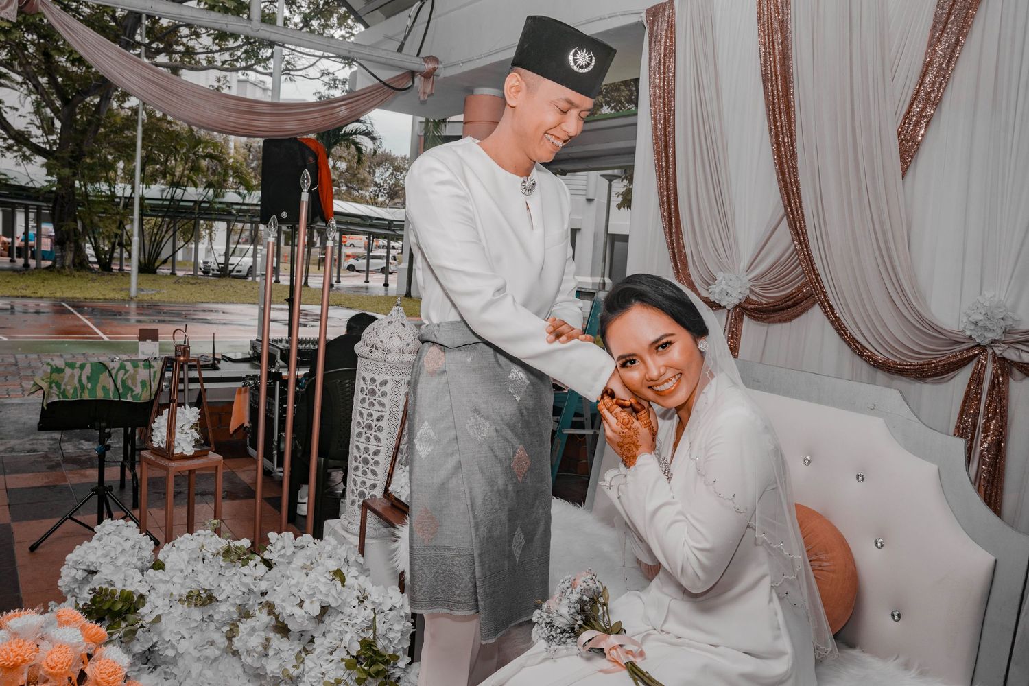 A wedding couple posing together at their reception with elegant white draping in the background.