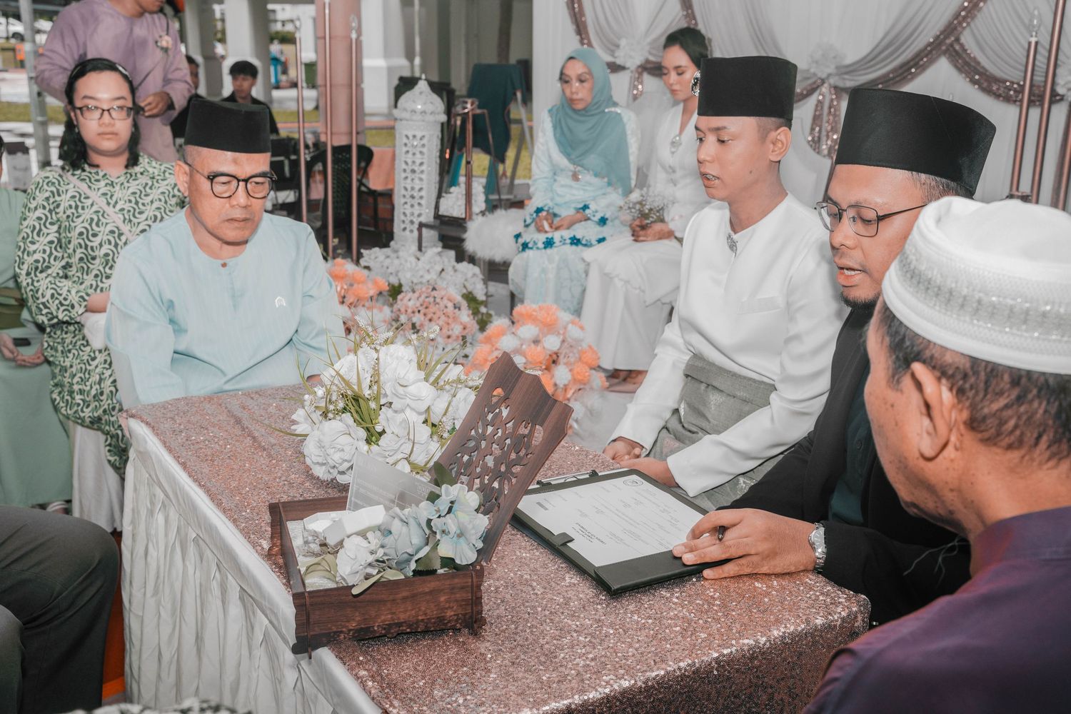 Traditional ceremony with participants seated at decorated table.