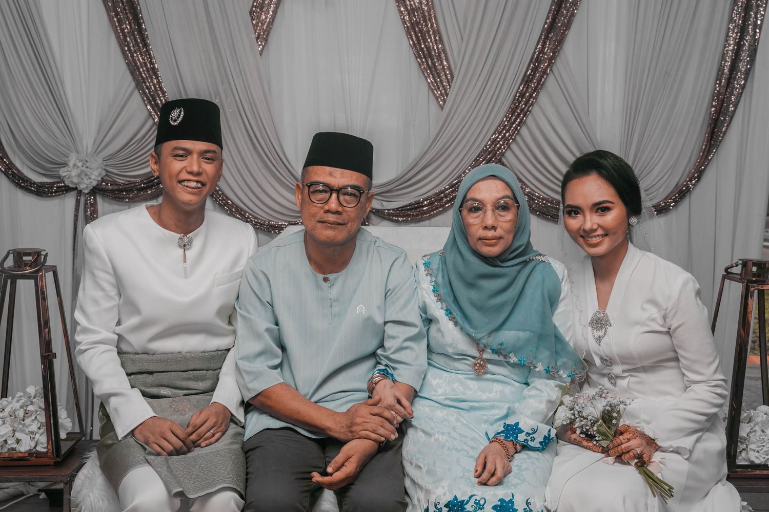 Family members gathered for a formal wedding portrait against draped white backdrop.
