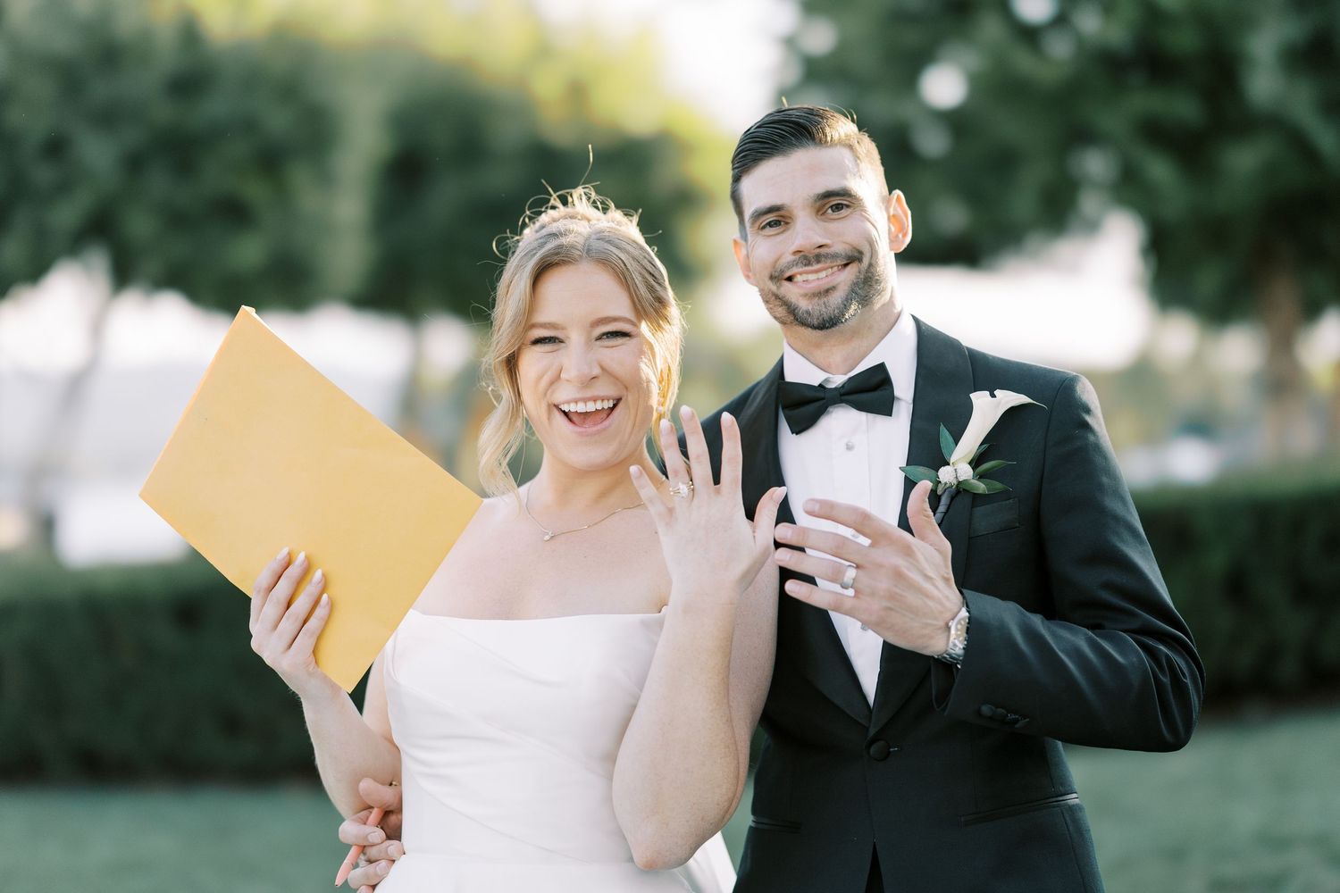 Newlywed couple sharing a joyful moment reading from yellow cards in an outdoor garden setting together.