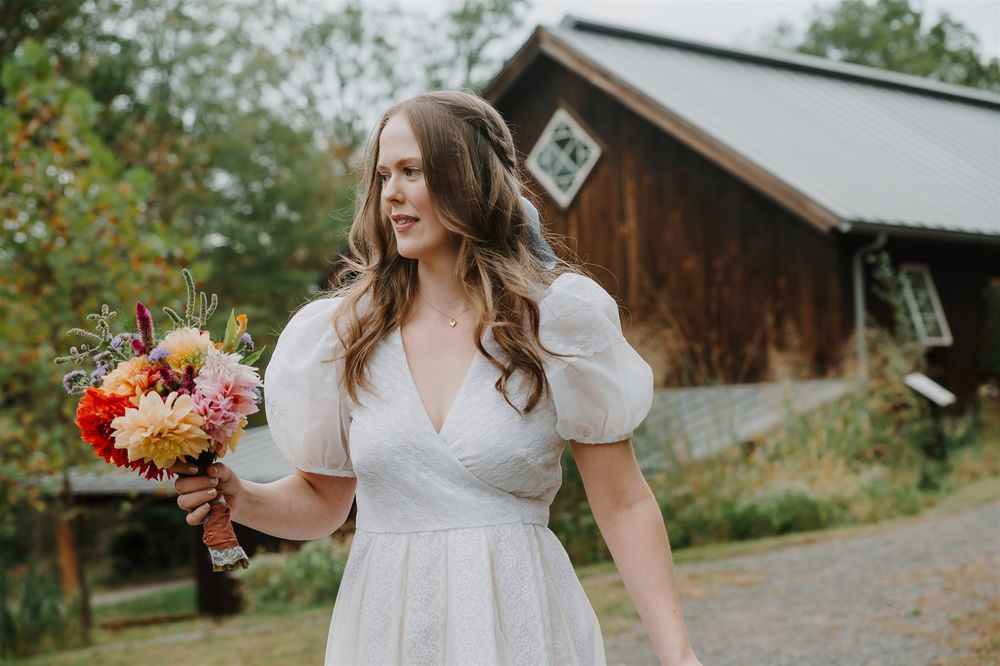 A bride wearing a flowing white wedding dress poses with an autumn flower bouquet in woodland setting.