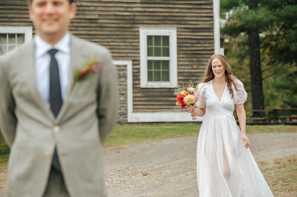 A happy couple celebrates their outdoor wedding on a fall day in front of a rustic wooden building.