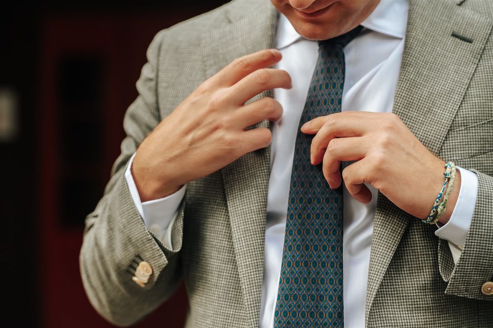 Close up detail of hands adjusting a polka dot tie with light gray suit jacket and white dress shirt.