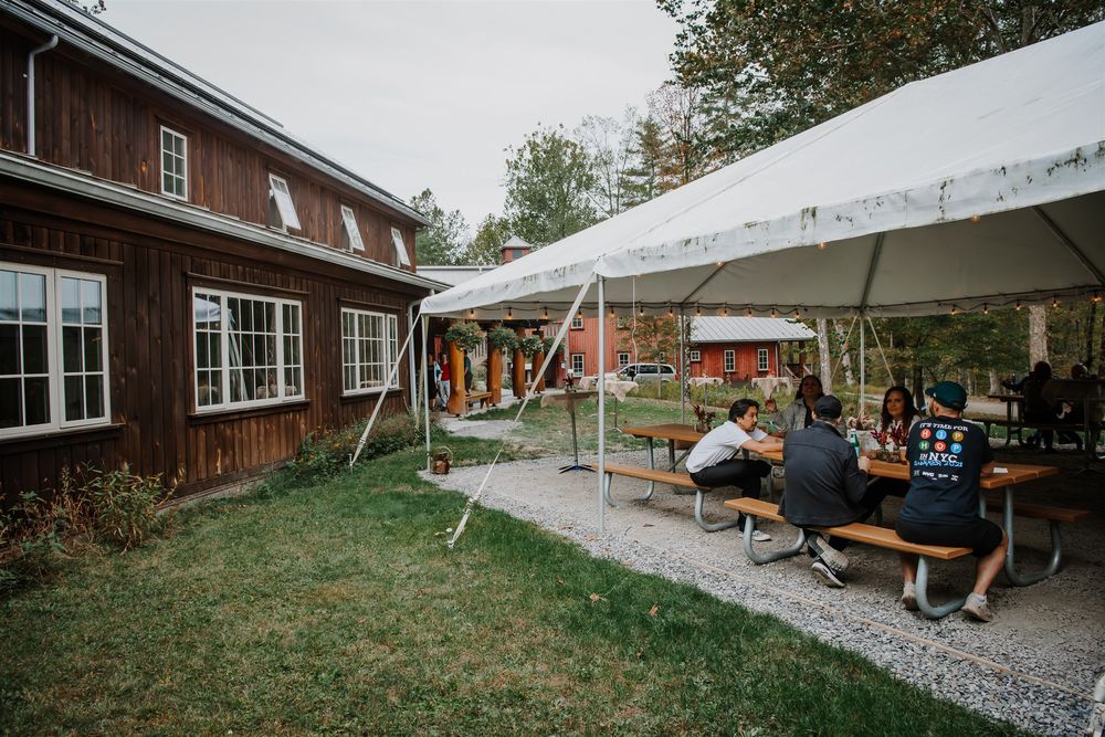 A panoramic view of a rustic barn venue with white tents and outdoor seating in a grassy field.