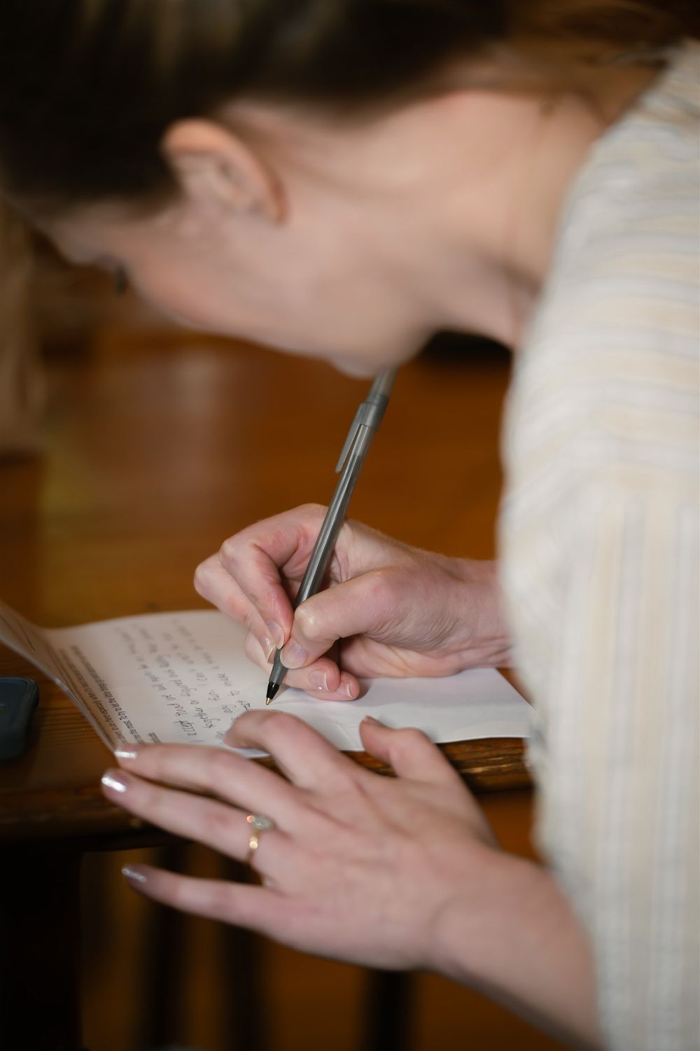 Close-up image of hands writing on paper with a pen in a soft, natural light setting.