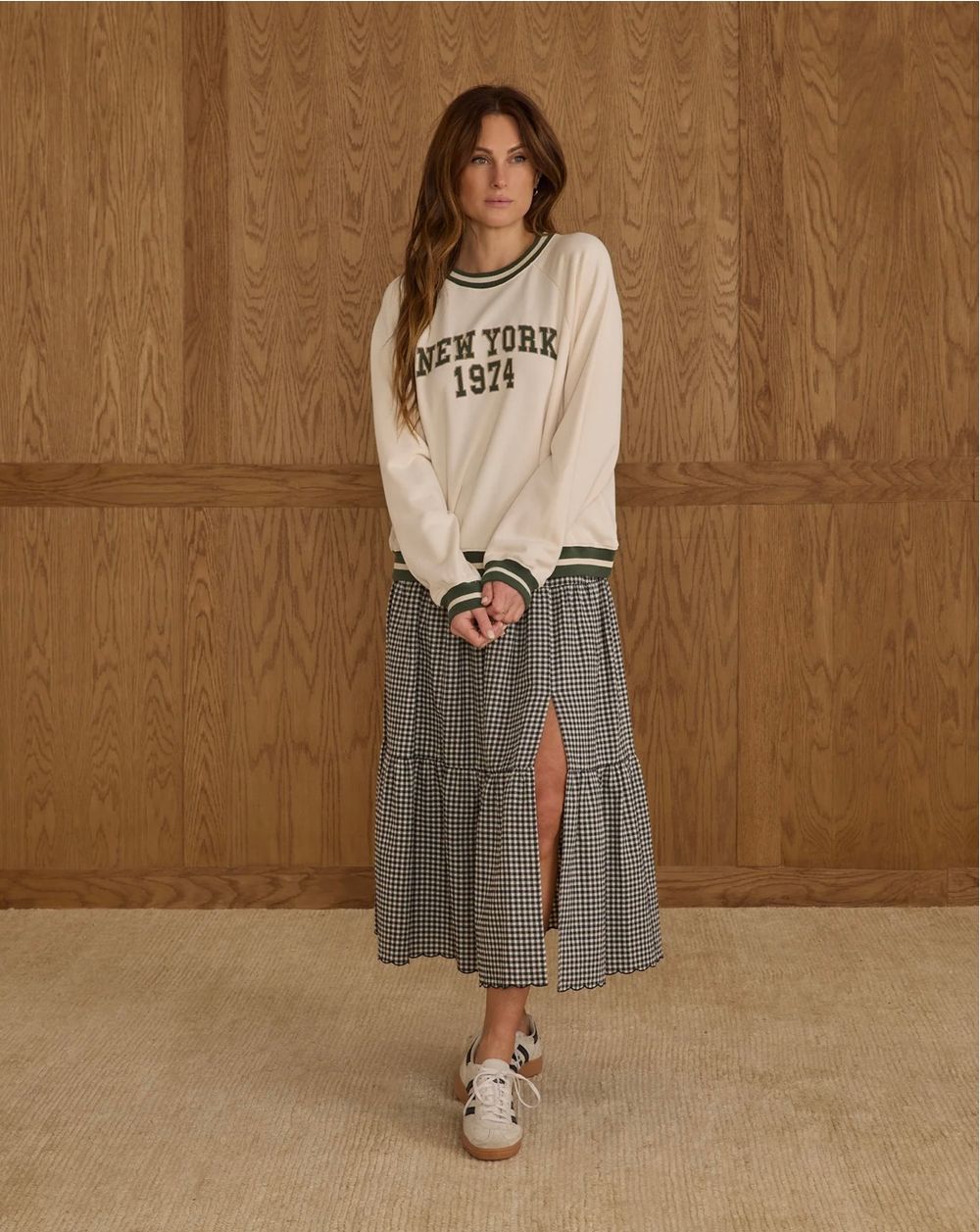 A person wearing a vintage-inspired white and grey plaid dress with New York text and sneakers in a warm-toned setting.