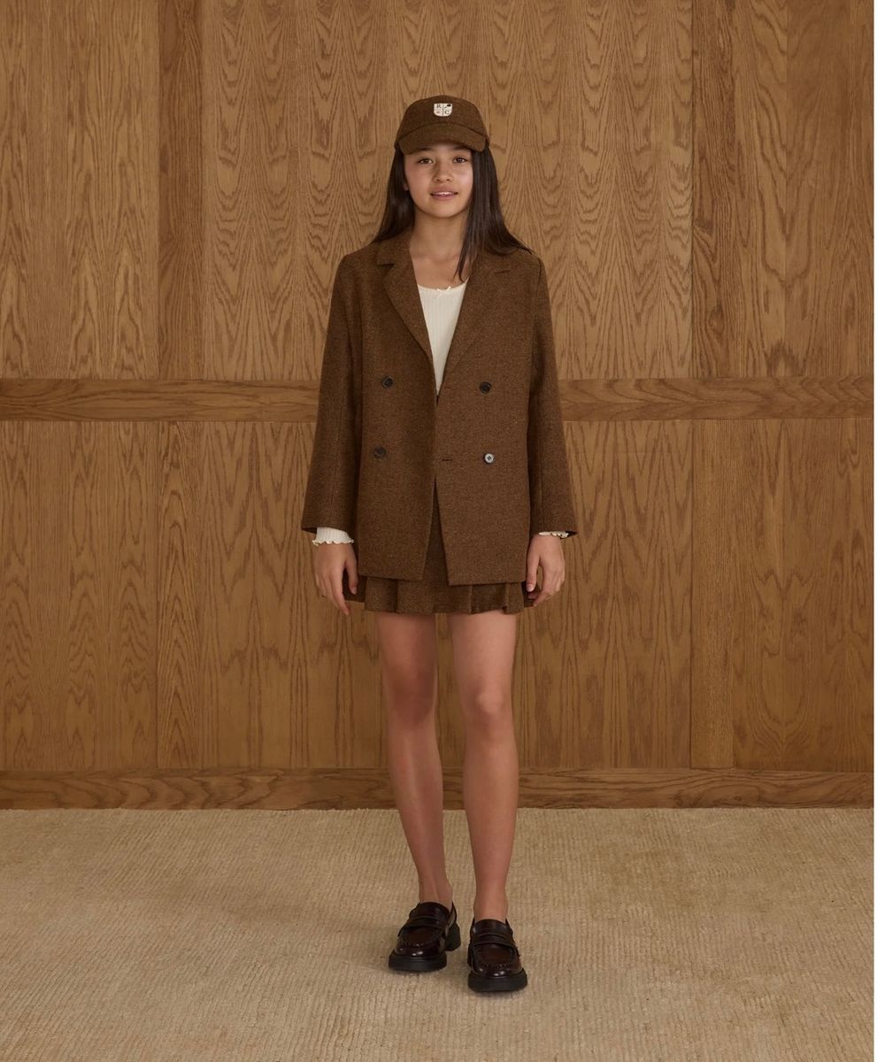 Five side-by-side images showing a person wearing a brown corduroy blazer styled with shorts and loafers on a beige carpet.