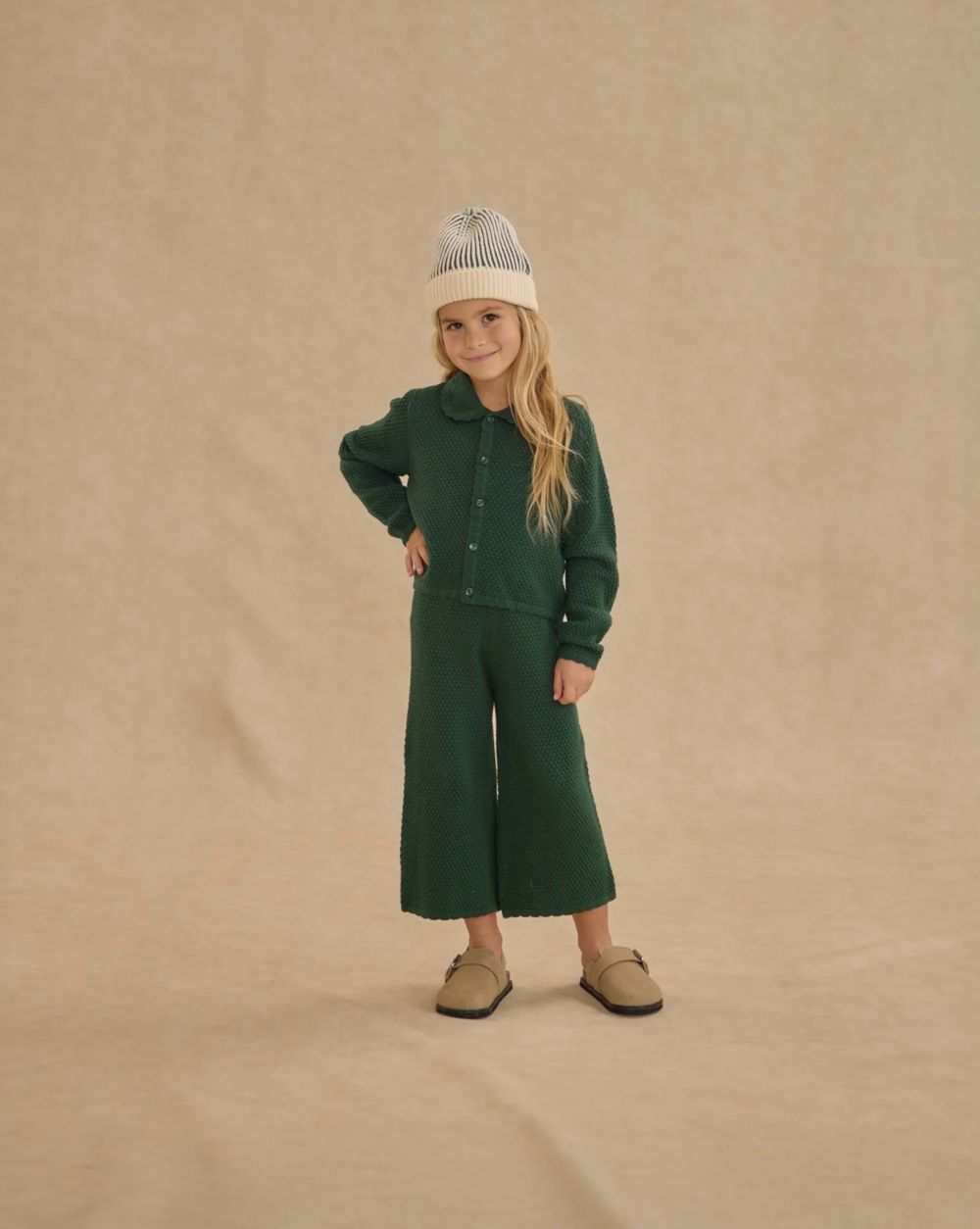 A set of five poses showing a green wool coat styled with beige boots on a neutral beige background.