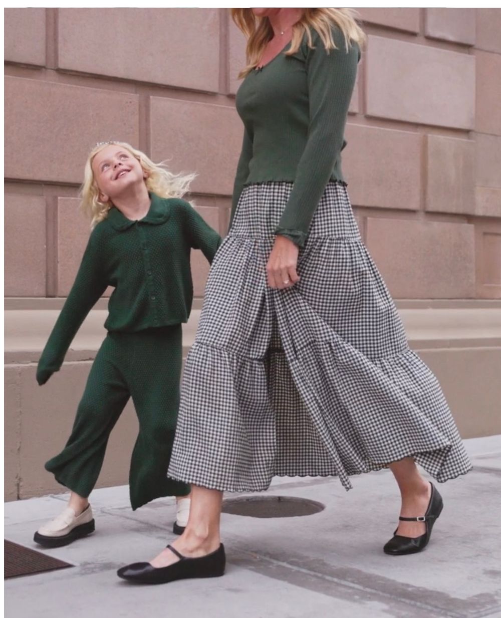 Two people in coordinating green and gingham outfits dancing playfully on city steps.
