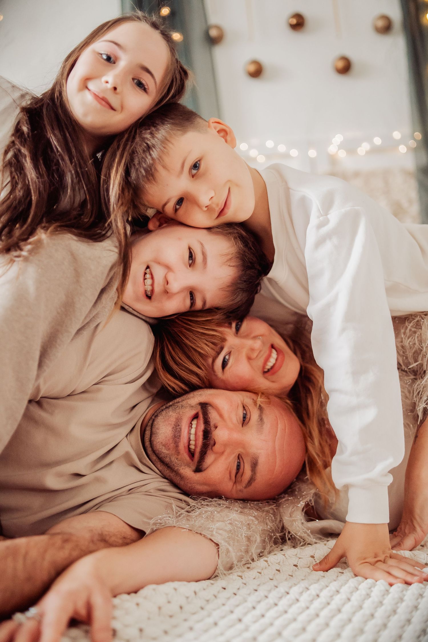 Happy family of five stacking heads together, smiling during a cozy Christmas photo session with festive lights.