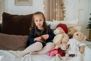 A series of five connected photos showing a young child with teddy bears and pillows in a bedroom setting.