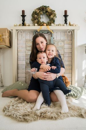 Intimate family lifestyle photo session on a plush white fur rug against a white brick wall background.