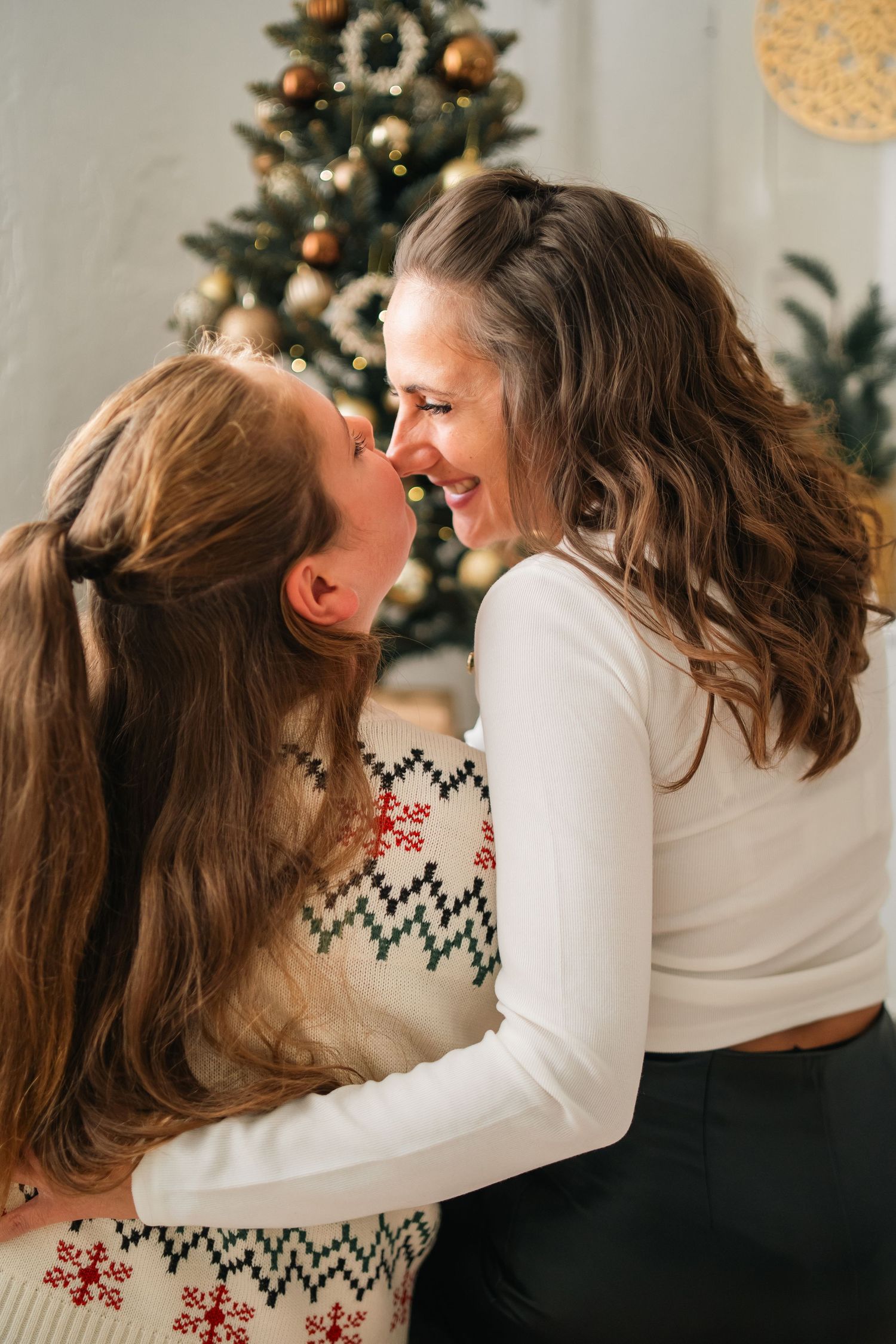 A loving couple shares intimate holiday moments in front of a decorated Christmas tree in matching white sweaters.