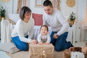 Happy family spending quality time together opening presents in a bright modern living room with Christmas gift boxes.