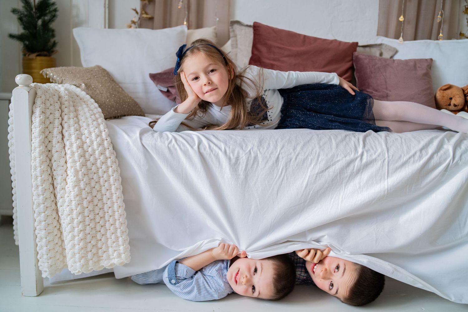 Children relaxing together on a cozy couch with white pillows and blankets in a living room setting.