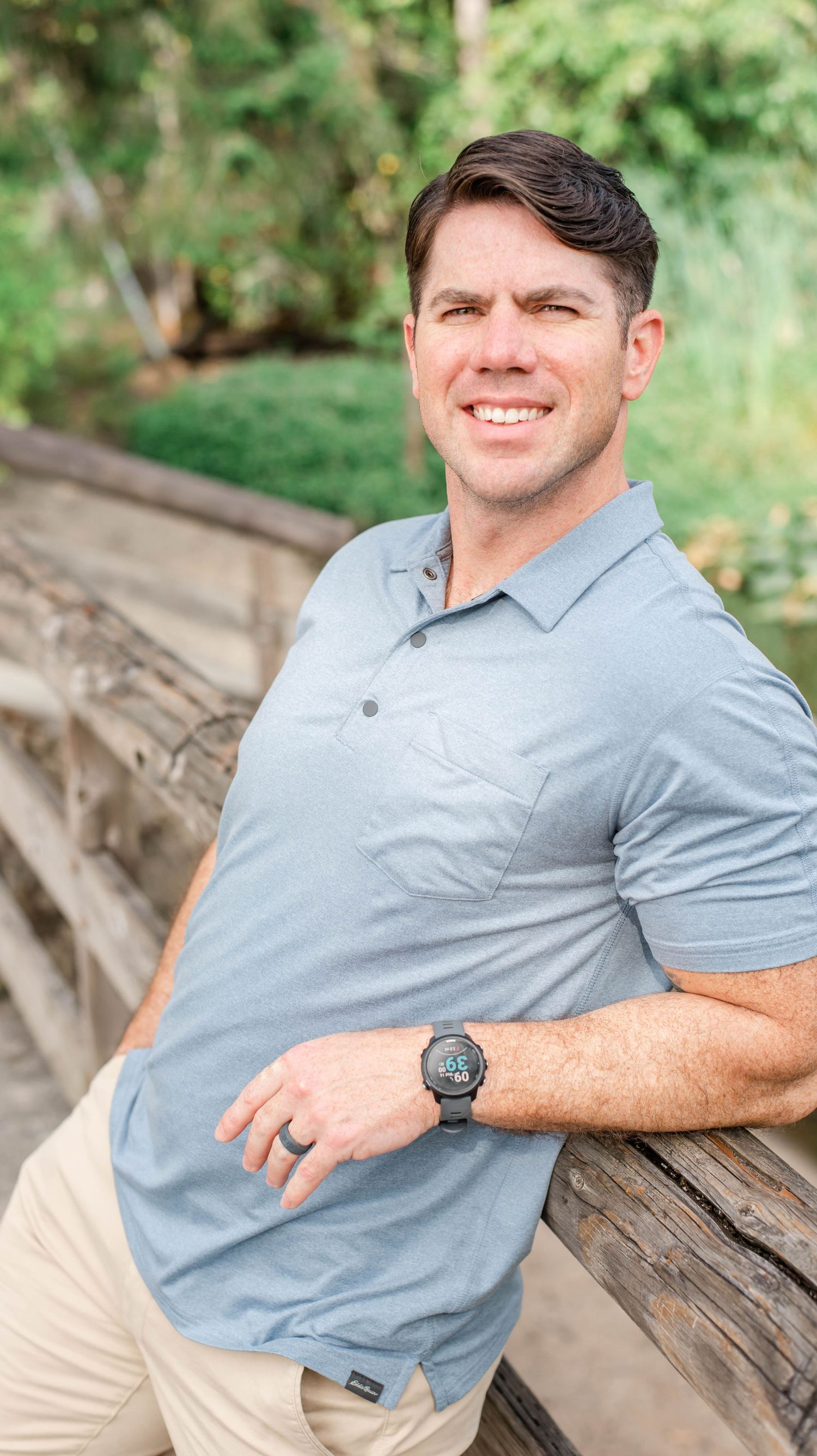 Person in gray polo shirt relaxing on wooden fence in sunny outdoor setting.