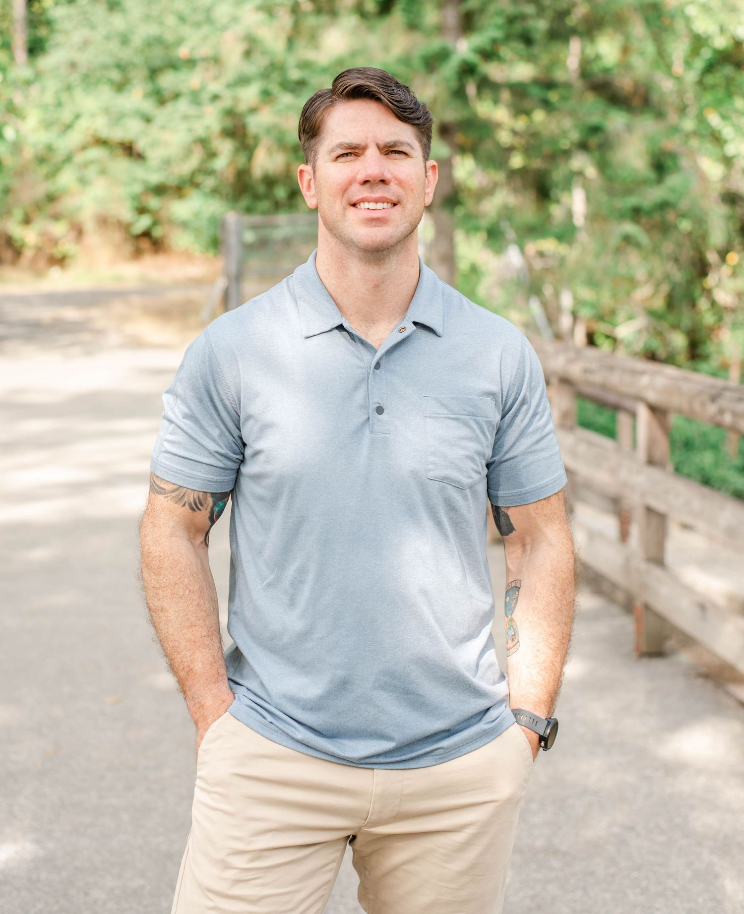 Person photographed in casual summer outfit stands beside wooden railing on outdoor path.