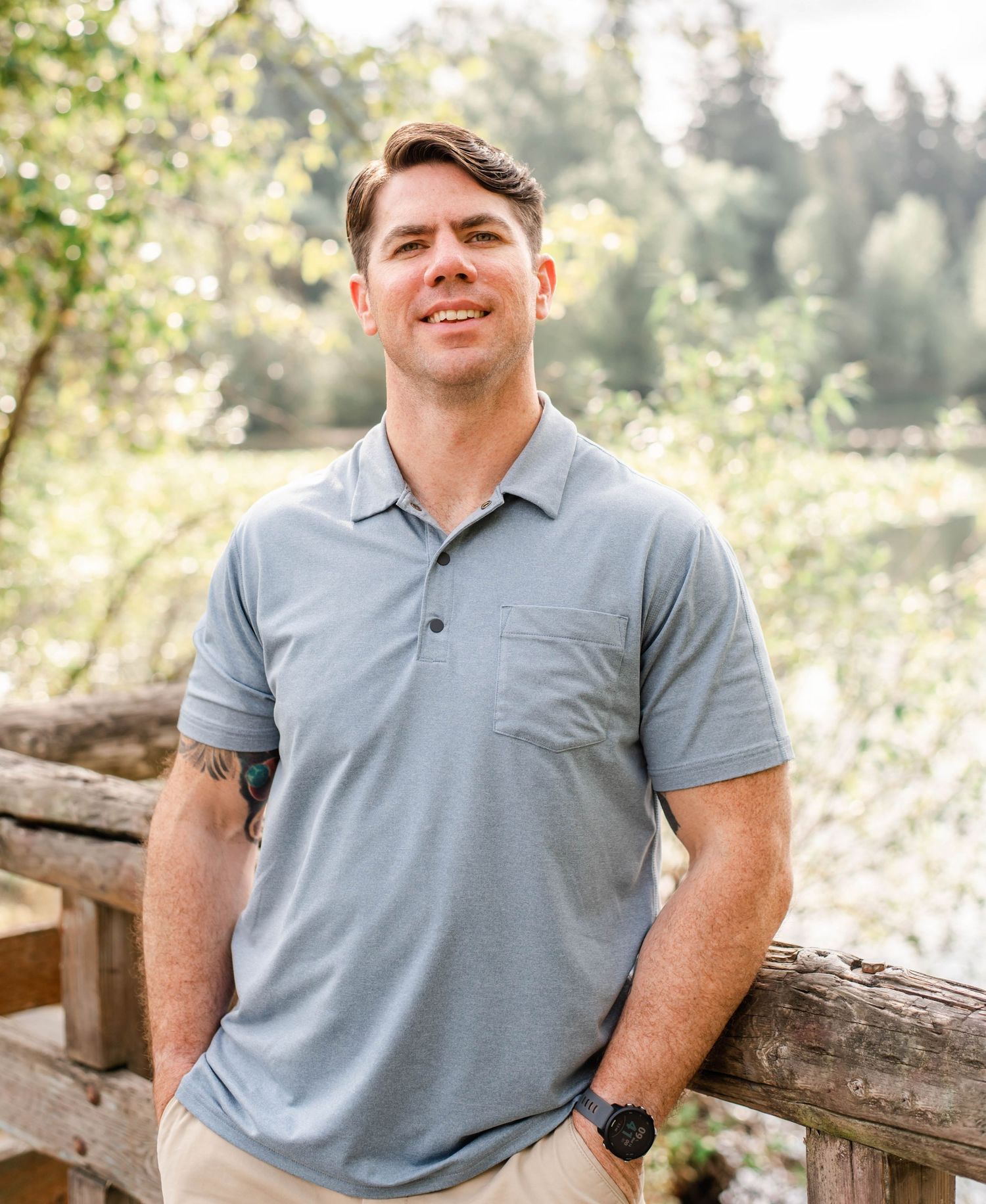 Person in short-sleeve polo relaxes against wooden fence in dappled sunlight.