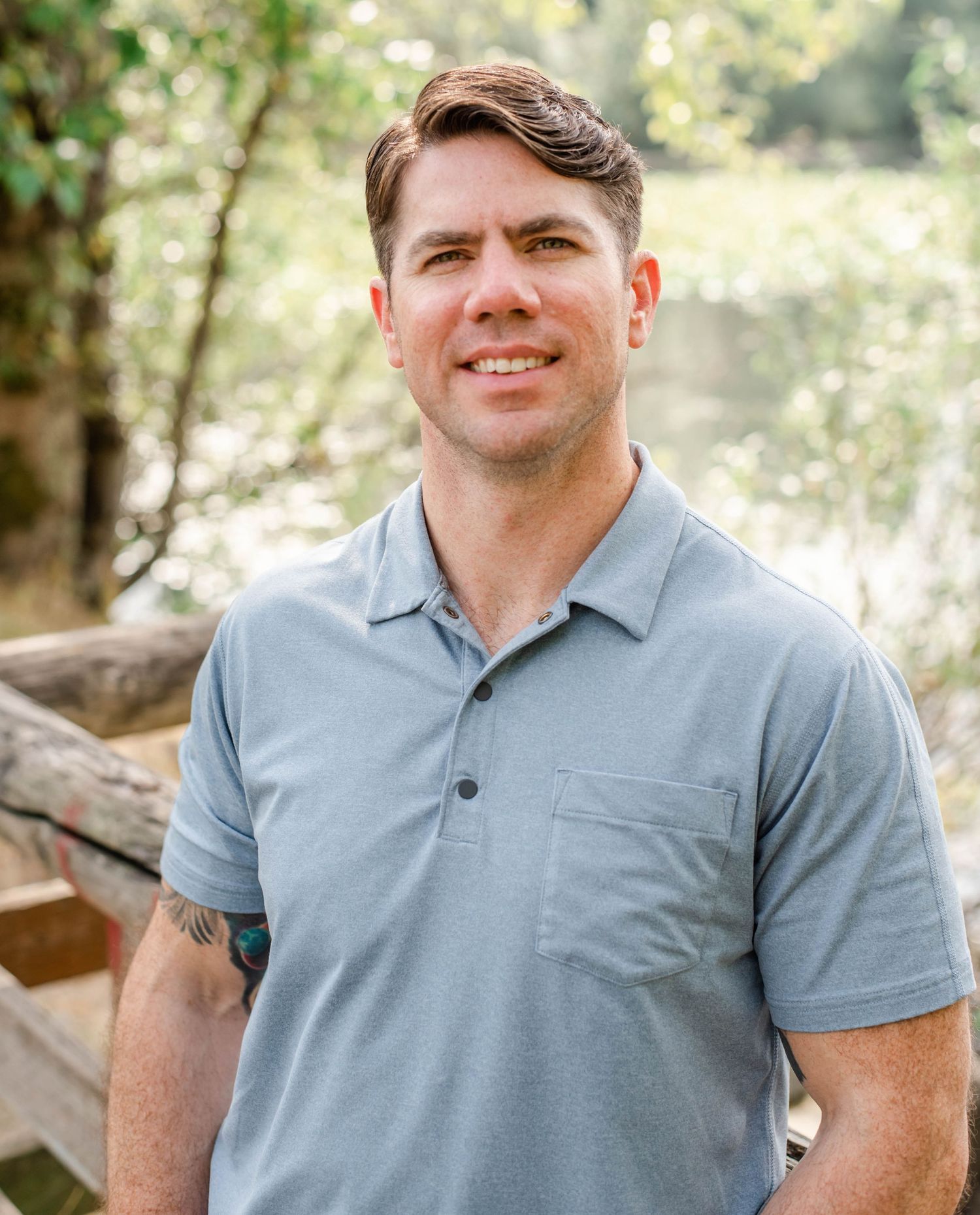 Casual portrait of person in light blue polo shirt against natural wooded background.