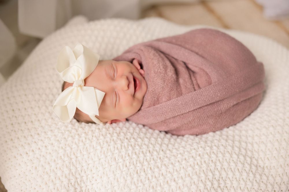Sleeping newborn wrapped in soft pink swaddle on textured cream blanket.