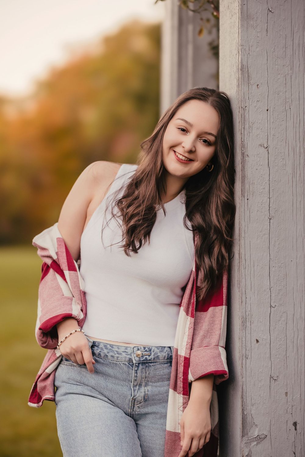 Lifestyle portrait against white column wearing casual denim and plaid outfit.