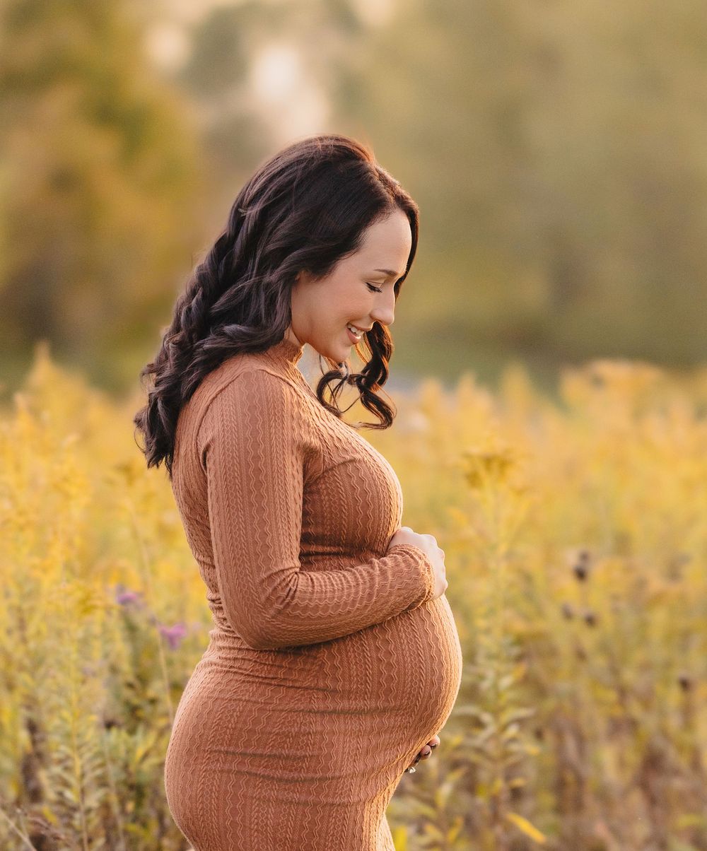 Maternity portraits in brown knit dress surrounded by golden autumn field.