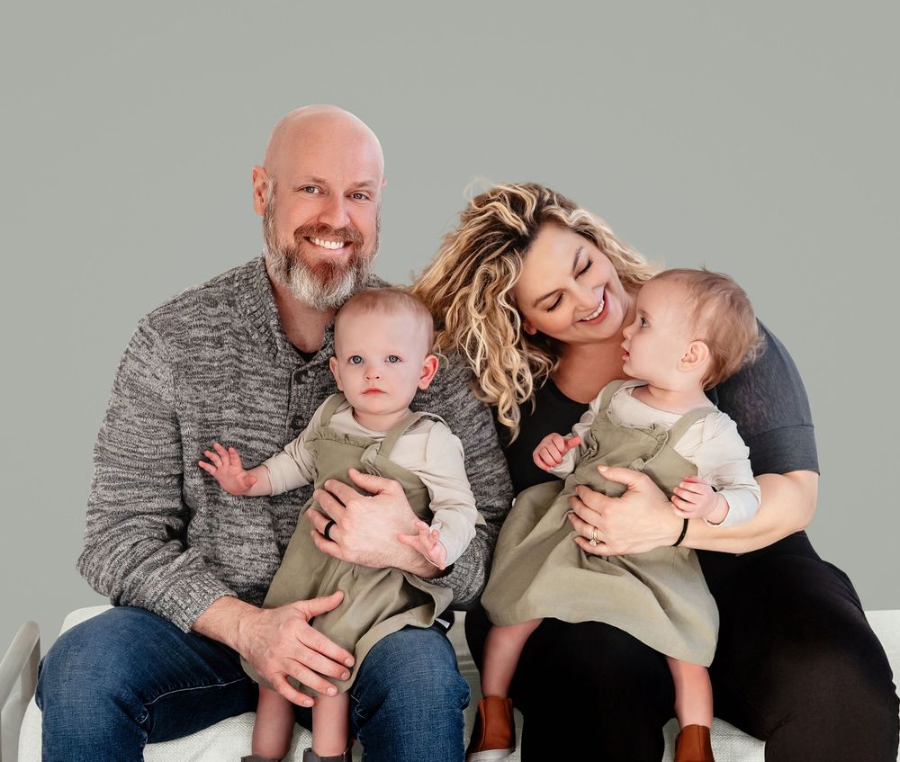 Family group poses together on gray background wearing coordinated neutral outfits.