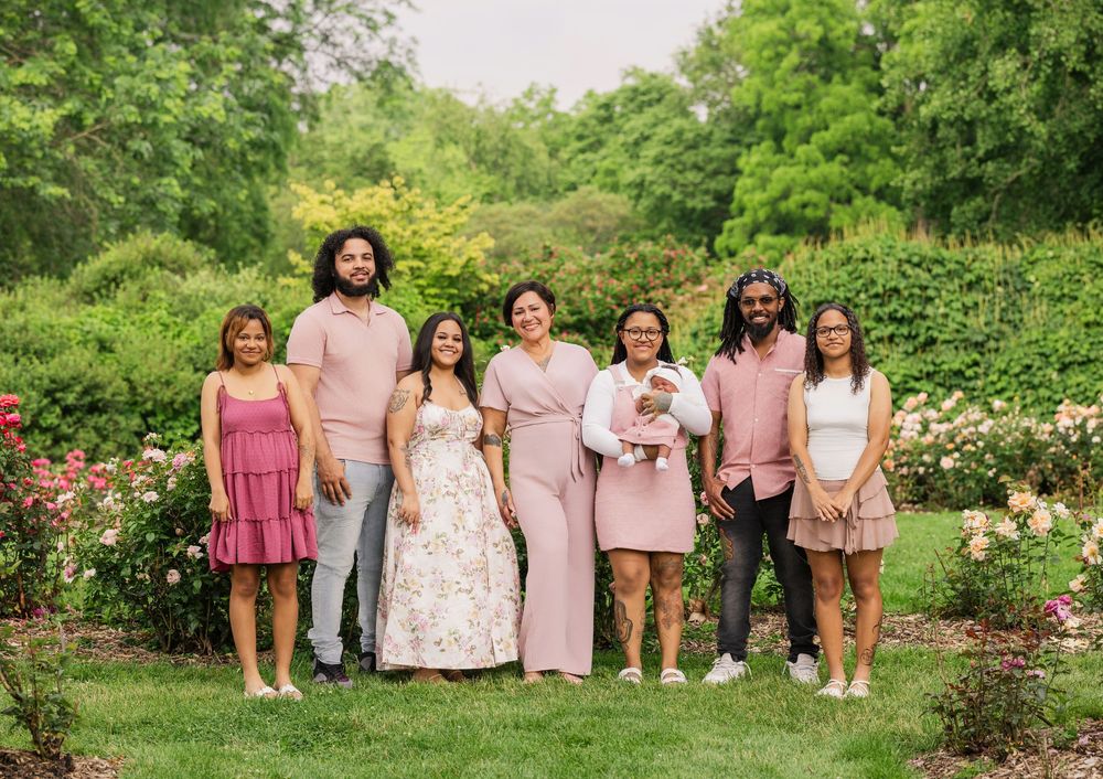 Group portrait in pink and floral dresses poses together in lush garden setting.