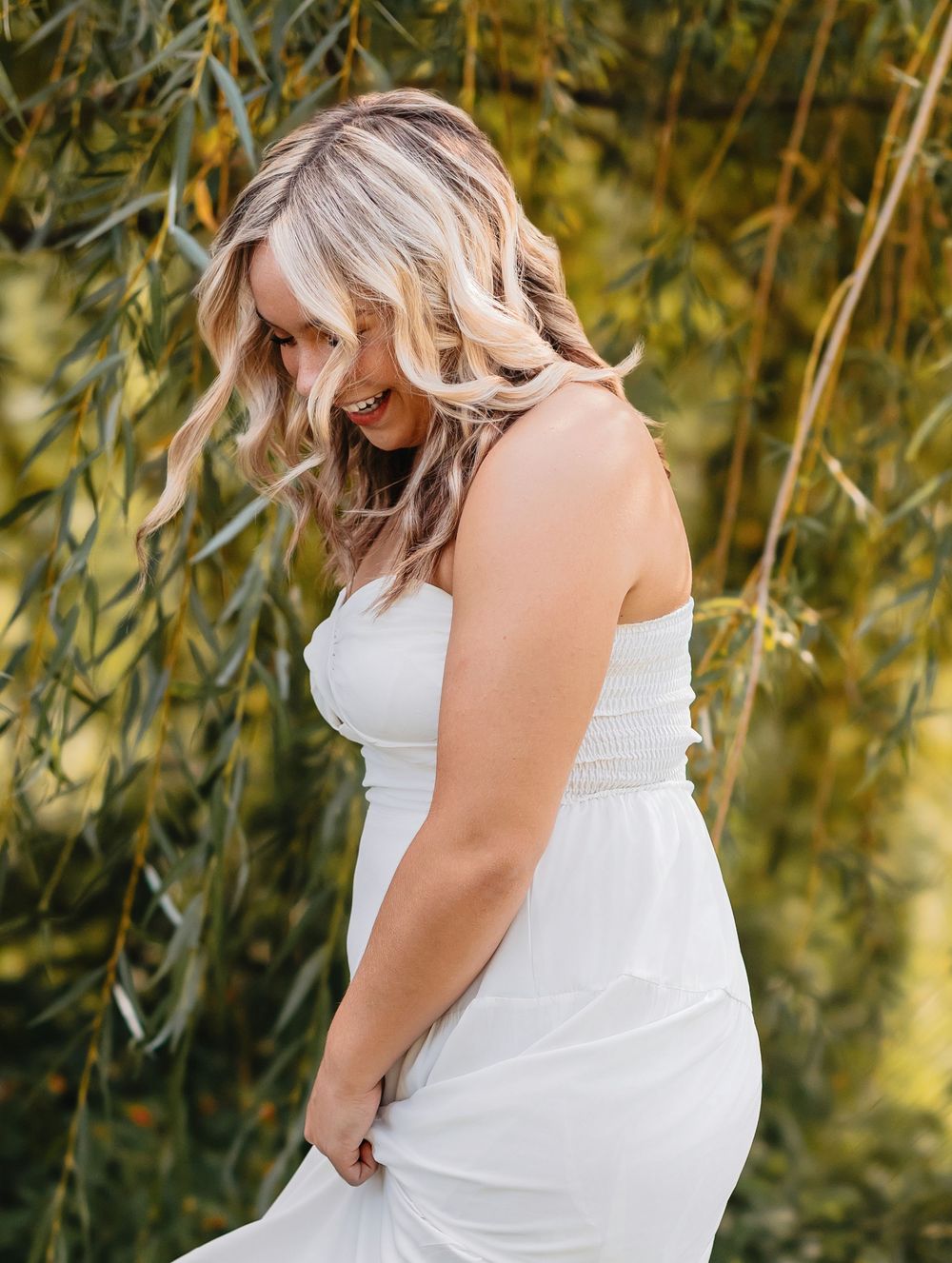 Elegant outdoor portrait session in white dress under weeping willow branches.