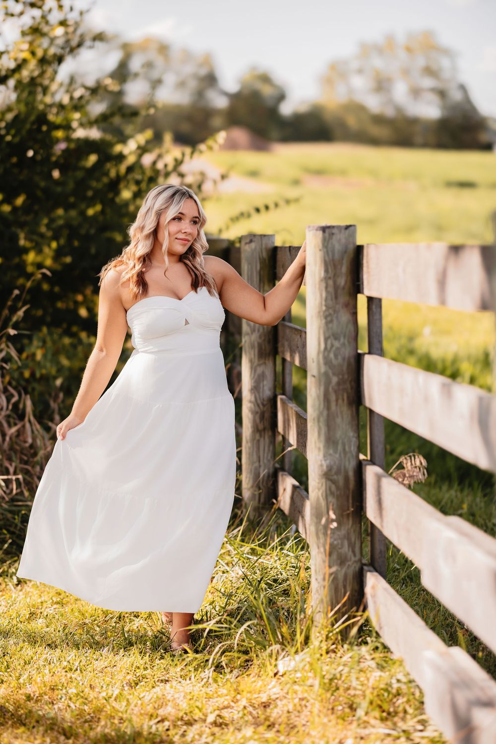 Ethereal summer photoshoot in white dress by rustic wooden fence.