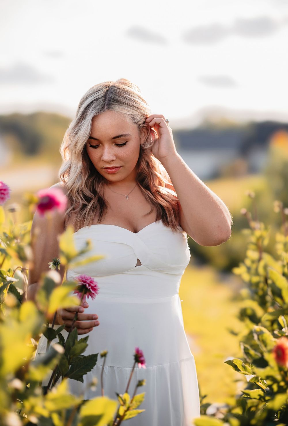 A white sundress contrasts beautifully against blooming pink and yellow wildflowers in a summer field at golden hour.