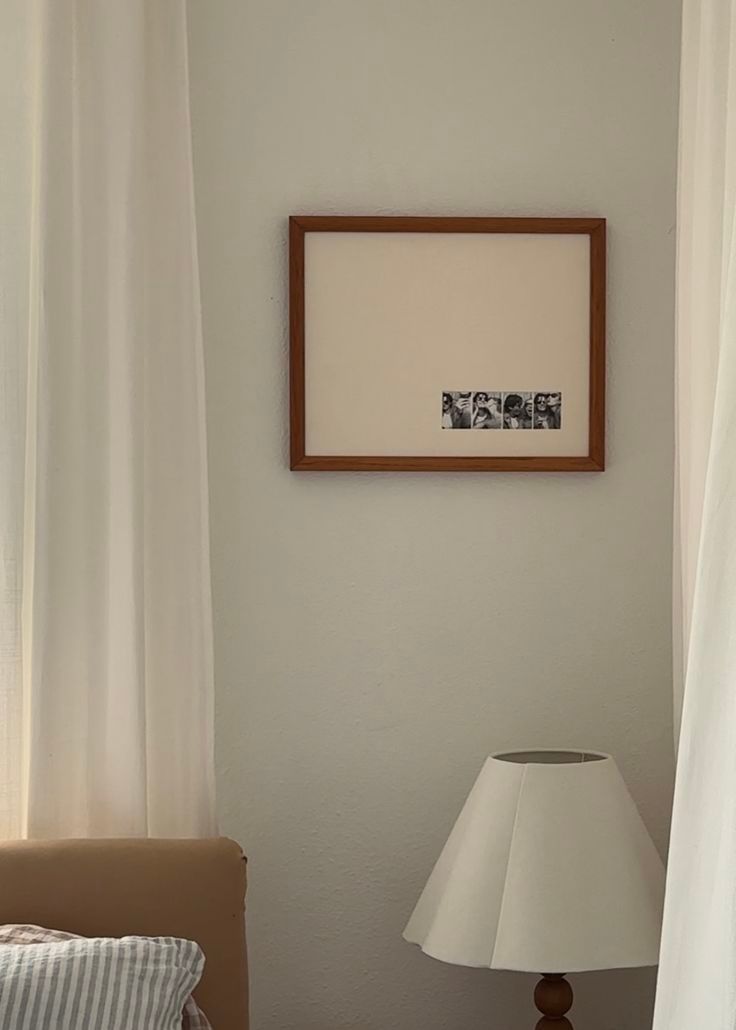 A modern living room interior with framed artwork, white curtains, table lamps, and a sleek minimalist design aesthetic.