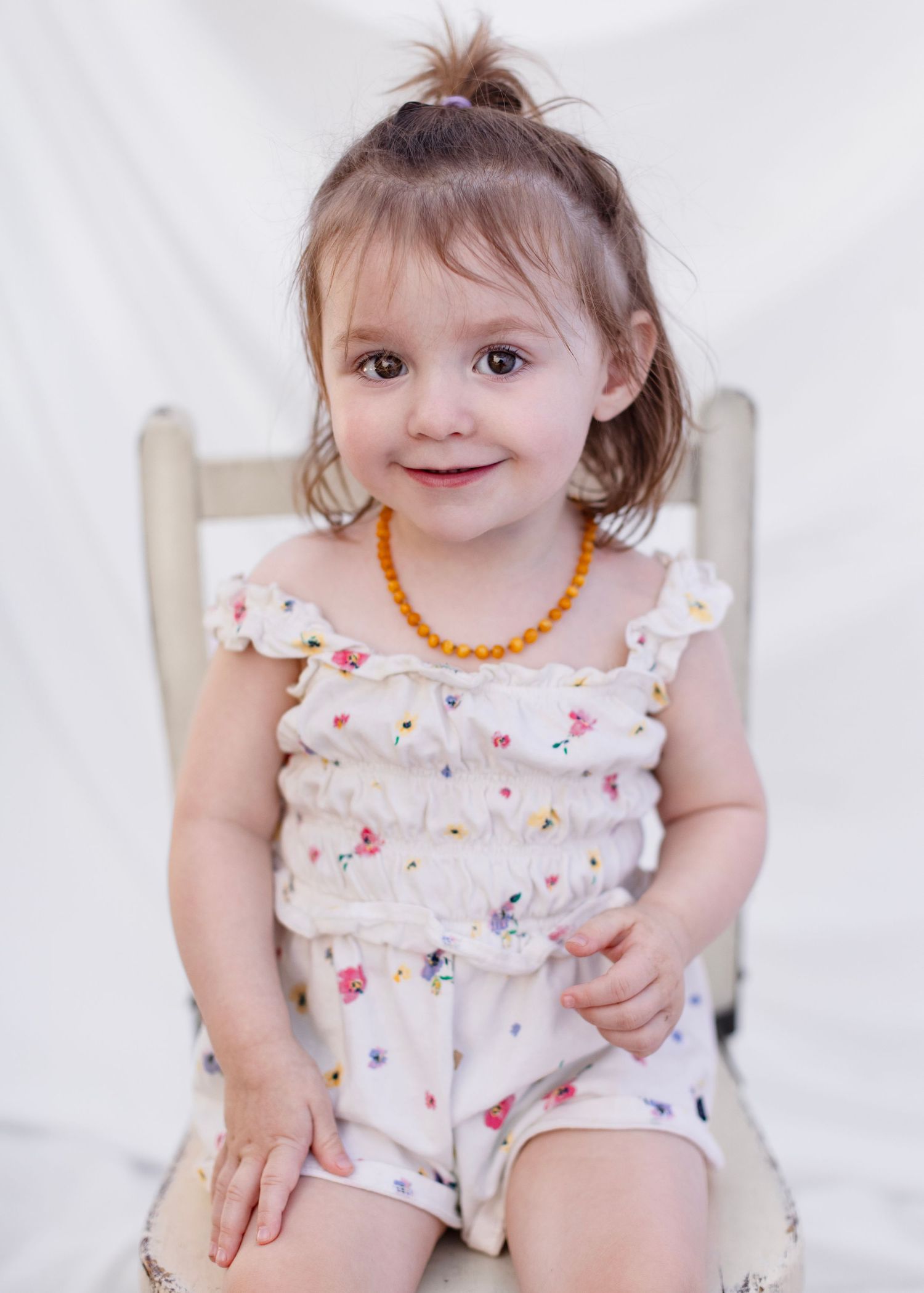 A toddler in a white floral dress with ruffled sleeves poses in multiple frames against a light background. Cloverdale Market Days